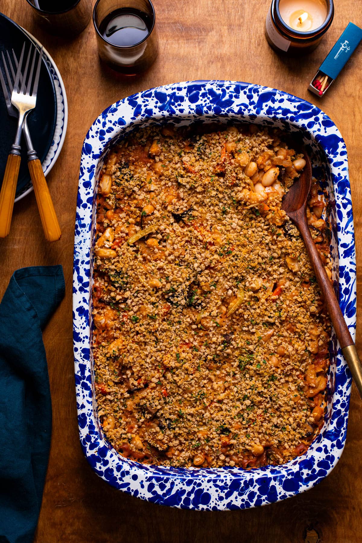 A glass Pyrex casserole dish of vegan cassoulet next to 2 ceramic plates on a beige tablecloth.
