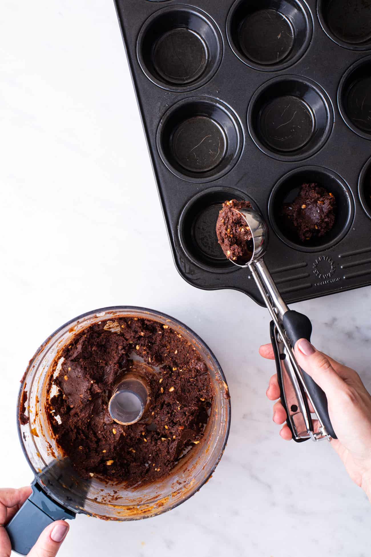 Woman's hand scooping brownie batter into muffin tin.