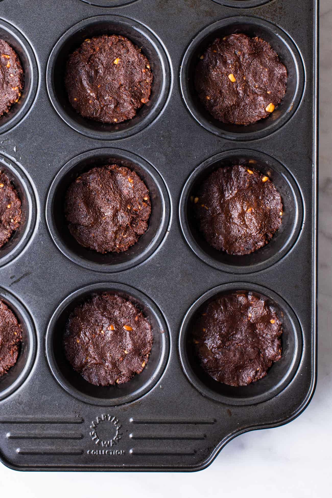 Vegan date brownies scooped into a muffin tin, ready to be baked.