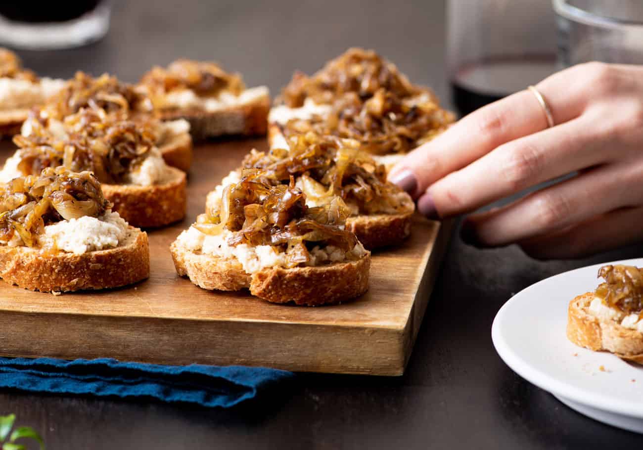 Balsamic caramelized onion crostini on a wooden board next to glasses with red wine