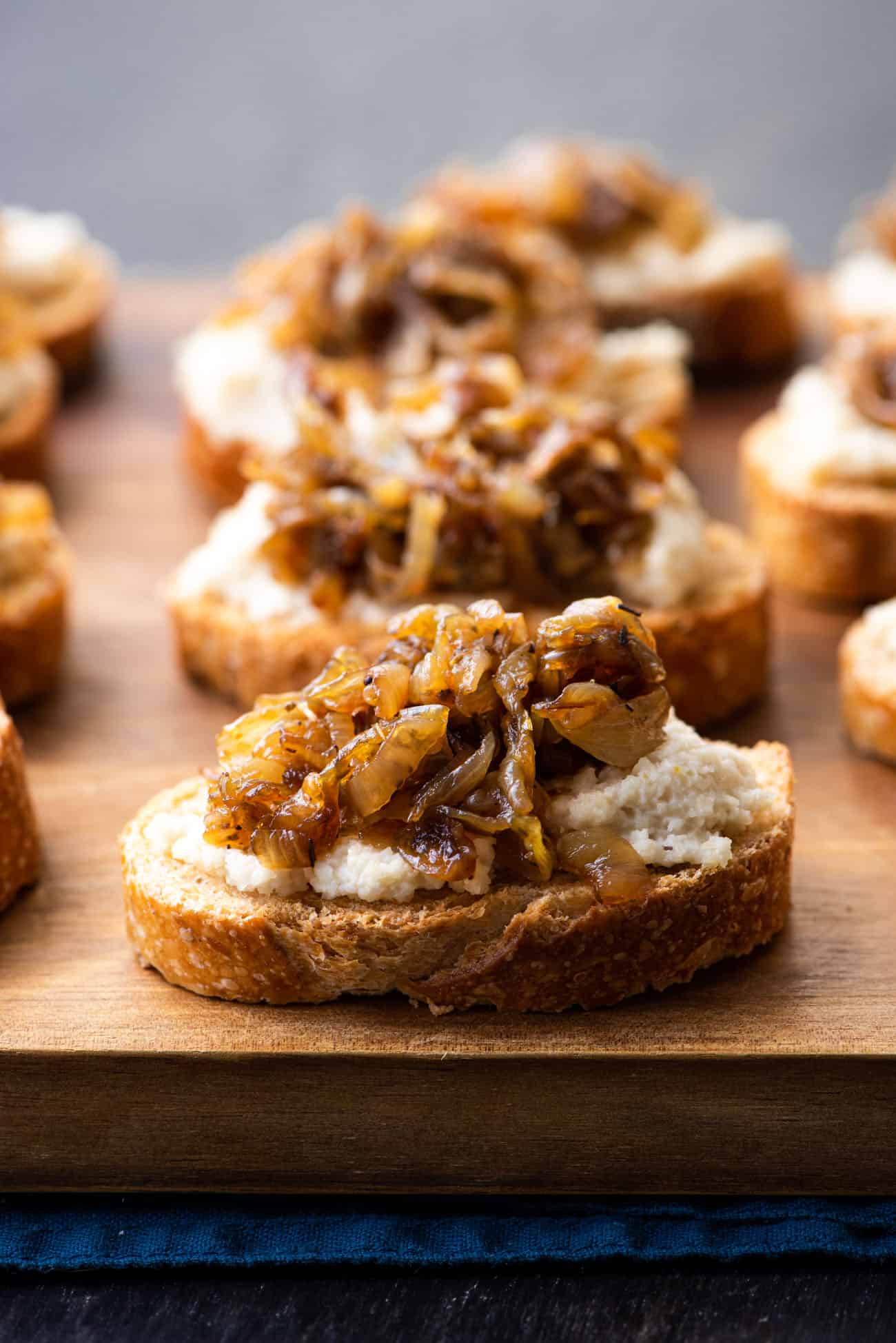 Caramelized onion crostini with cashew ricotta on a wooden board.