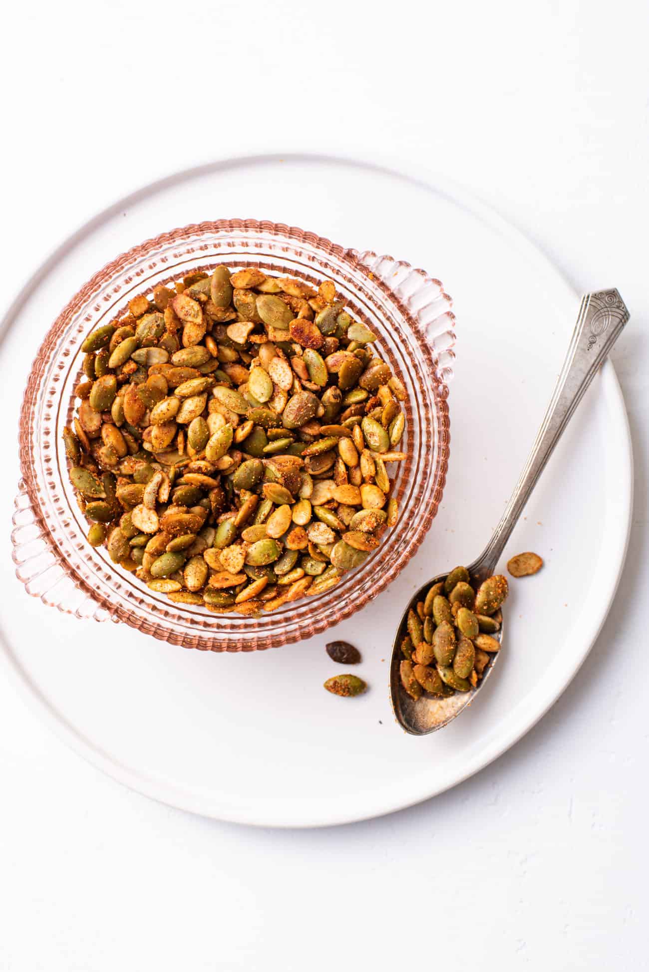 Spiced pumpkin seeds in a pink glass bowl on a white ceramic plate
