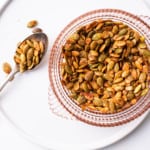 Spiced pumpkin seeds in a pink glass bowl on a white ceramic plate
