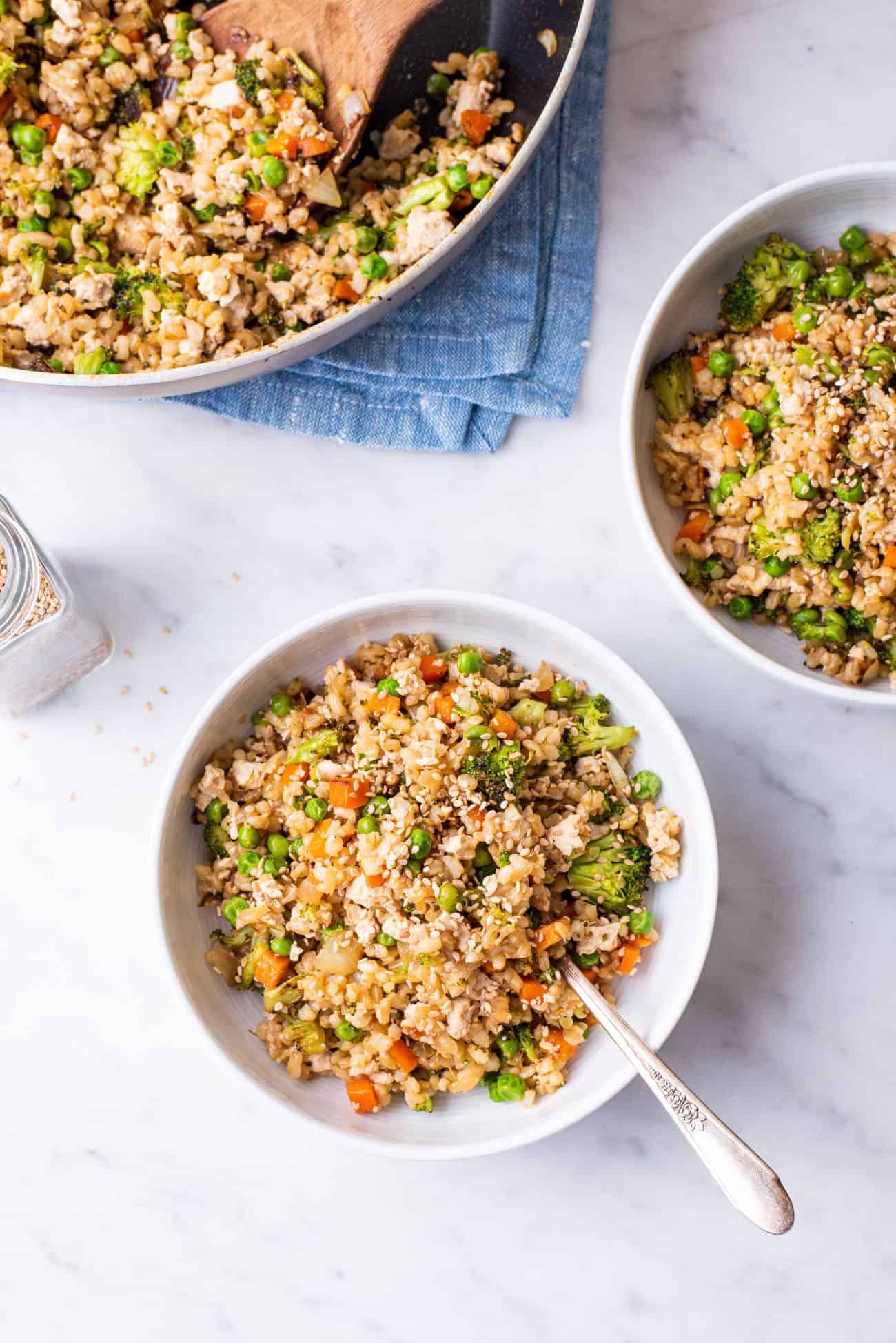 Two white bowls with vegetable fried brown rice on a marble table