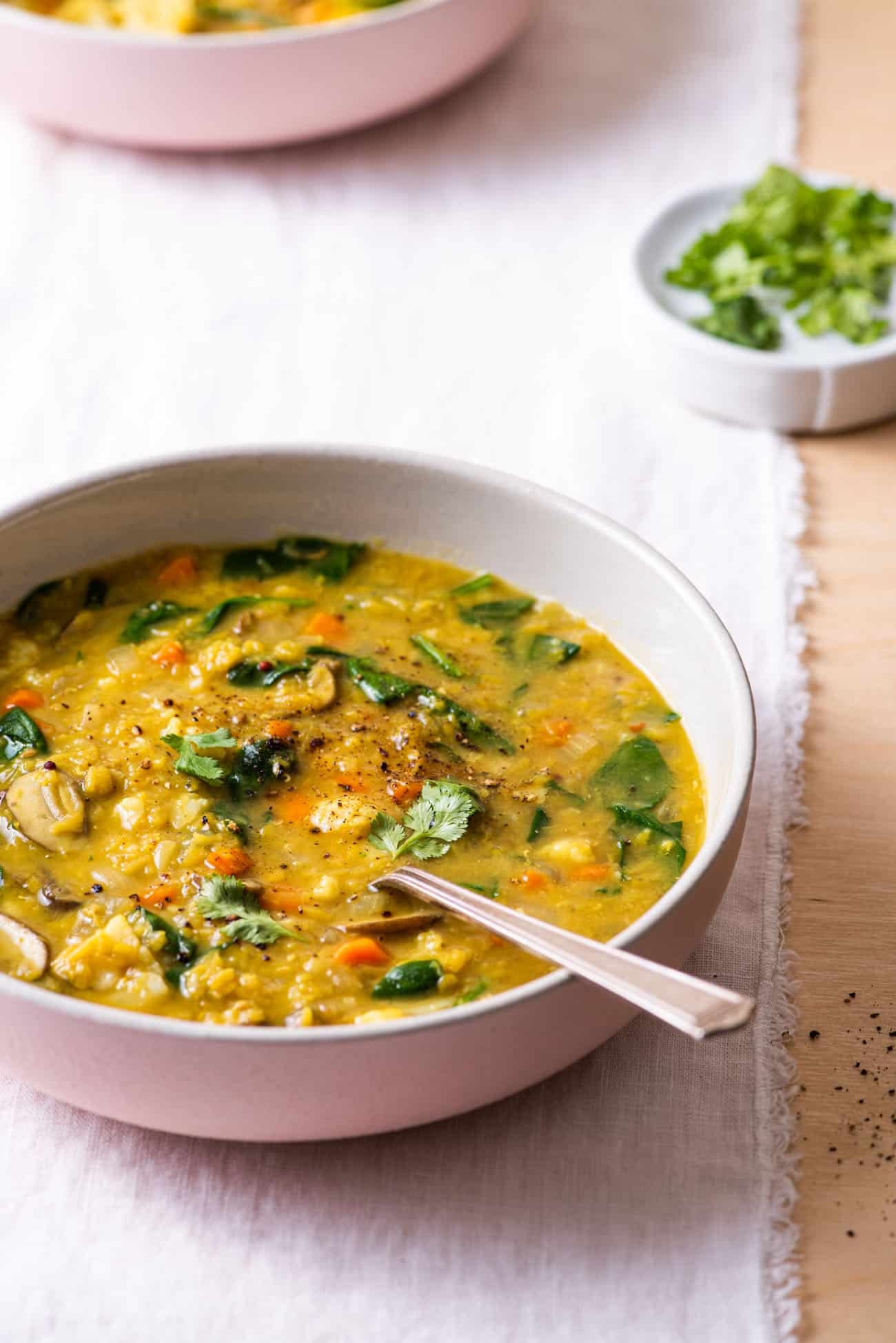 Indian red lentil dal with spinach in pink ceramic bowls.