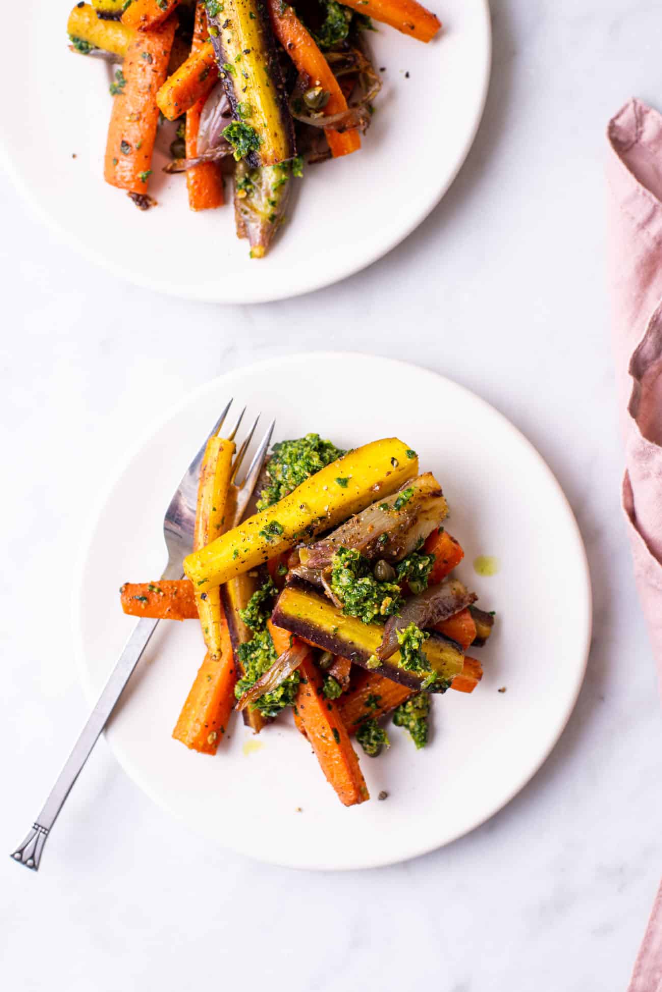 2 small white plates with roasted pesto carrots on a marble table