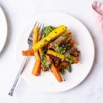 Roasted carrots and shallots with parsley pesto on a small white plate on a marble table