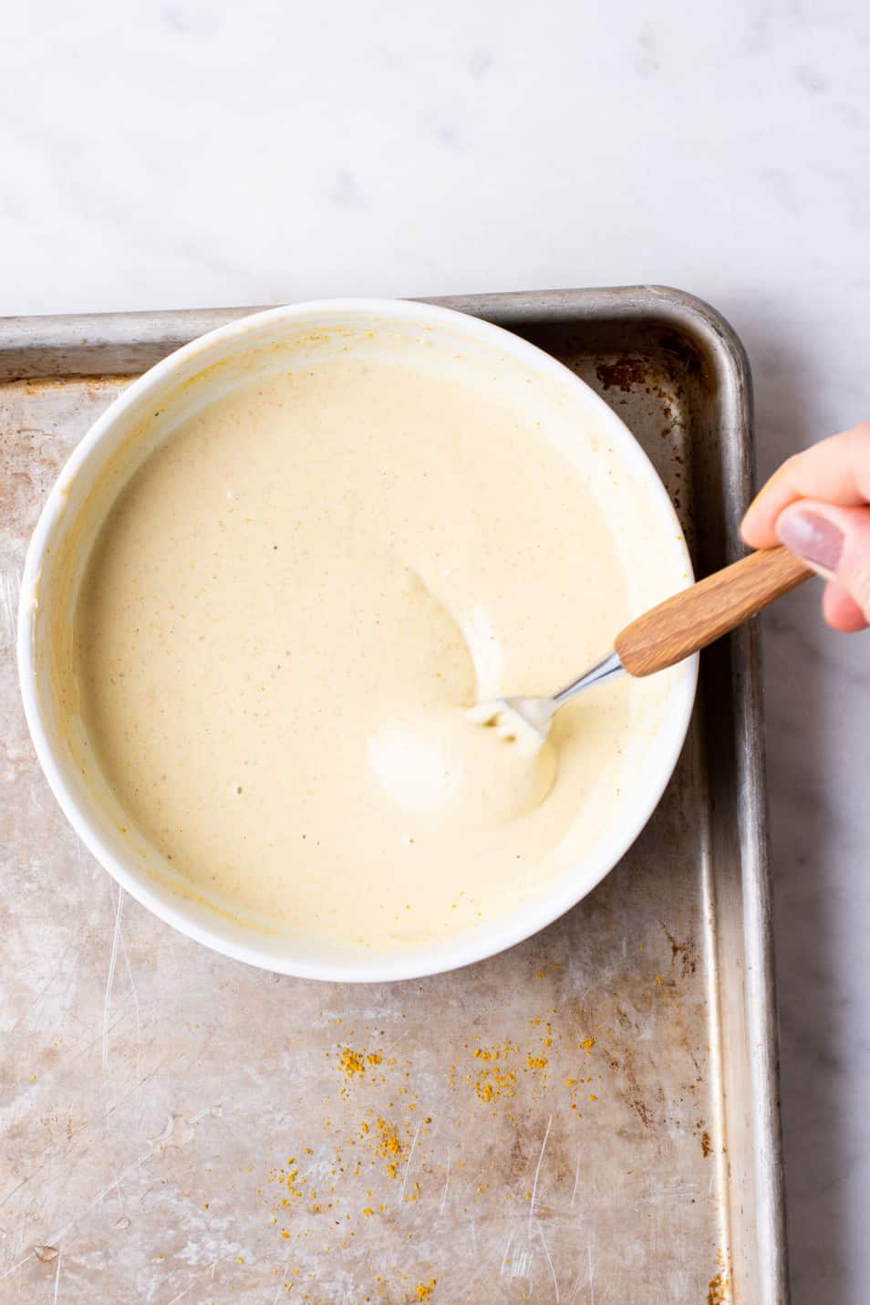 Woman's hand whisking curry tahini sauce with a fork.