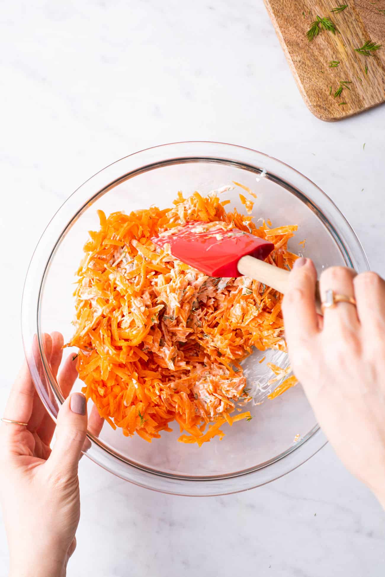 Woman's hands mixing a shredded carrot salad with a yogurt dressing in a glass bowl