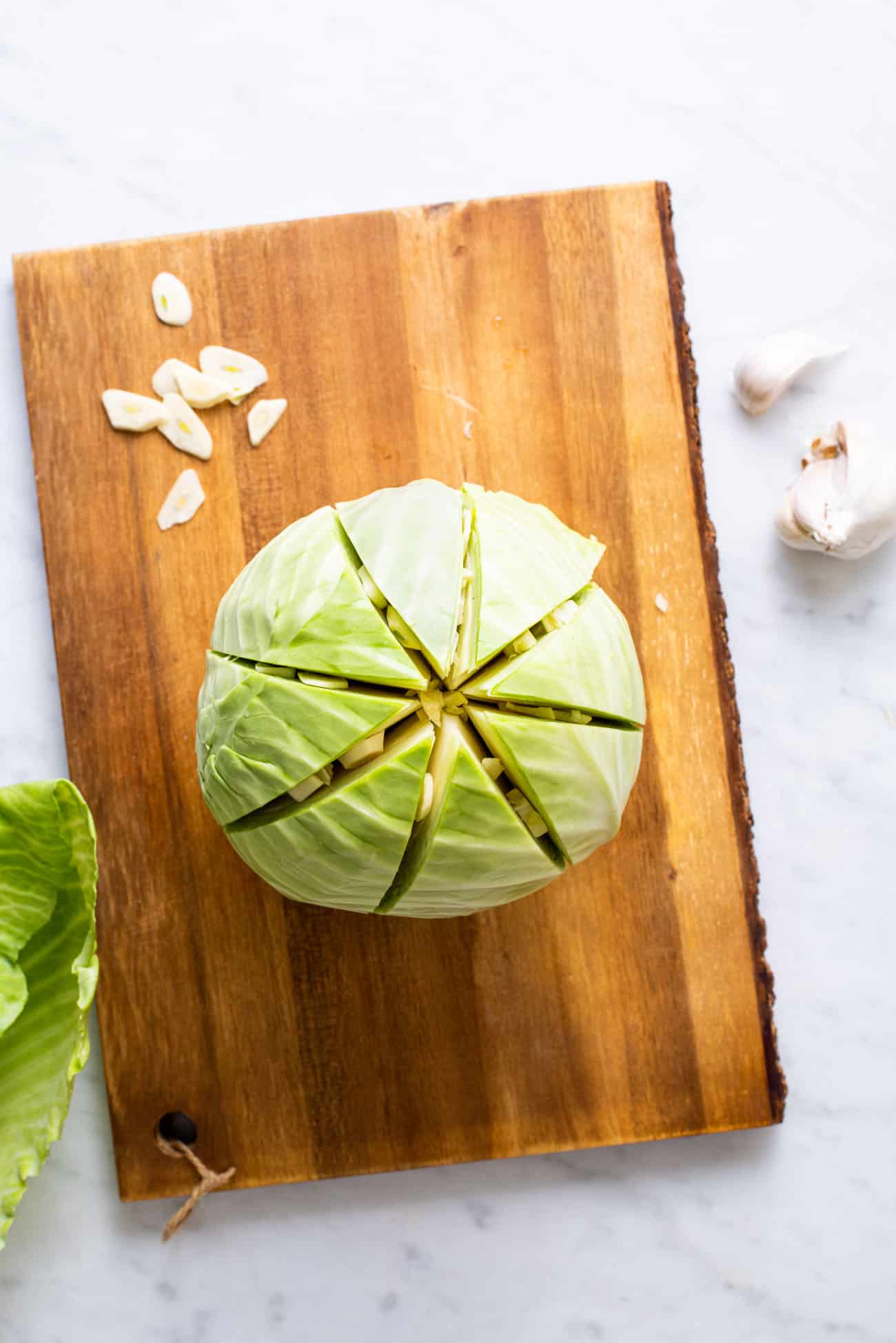 A scored raw cabbage on a cutting board with sliced garlic