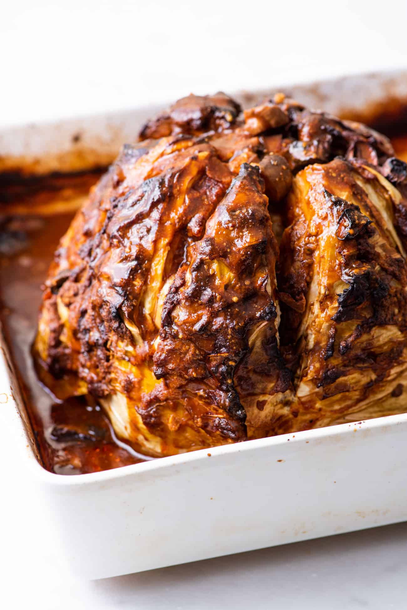 A saucy caramelized whole roasted cabbage in a square roasting pan