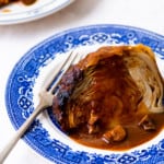 A wedge of whole roasted cabbage with a mushroom-tomato gravy drizzled on top, on a blue chinoiserie plate