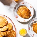 Banana walnut pancakes on a sunny table, next to glasses of orange juice, and blueberry chia jam