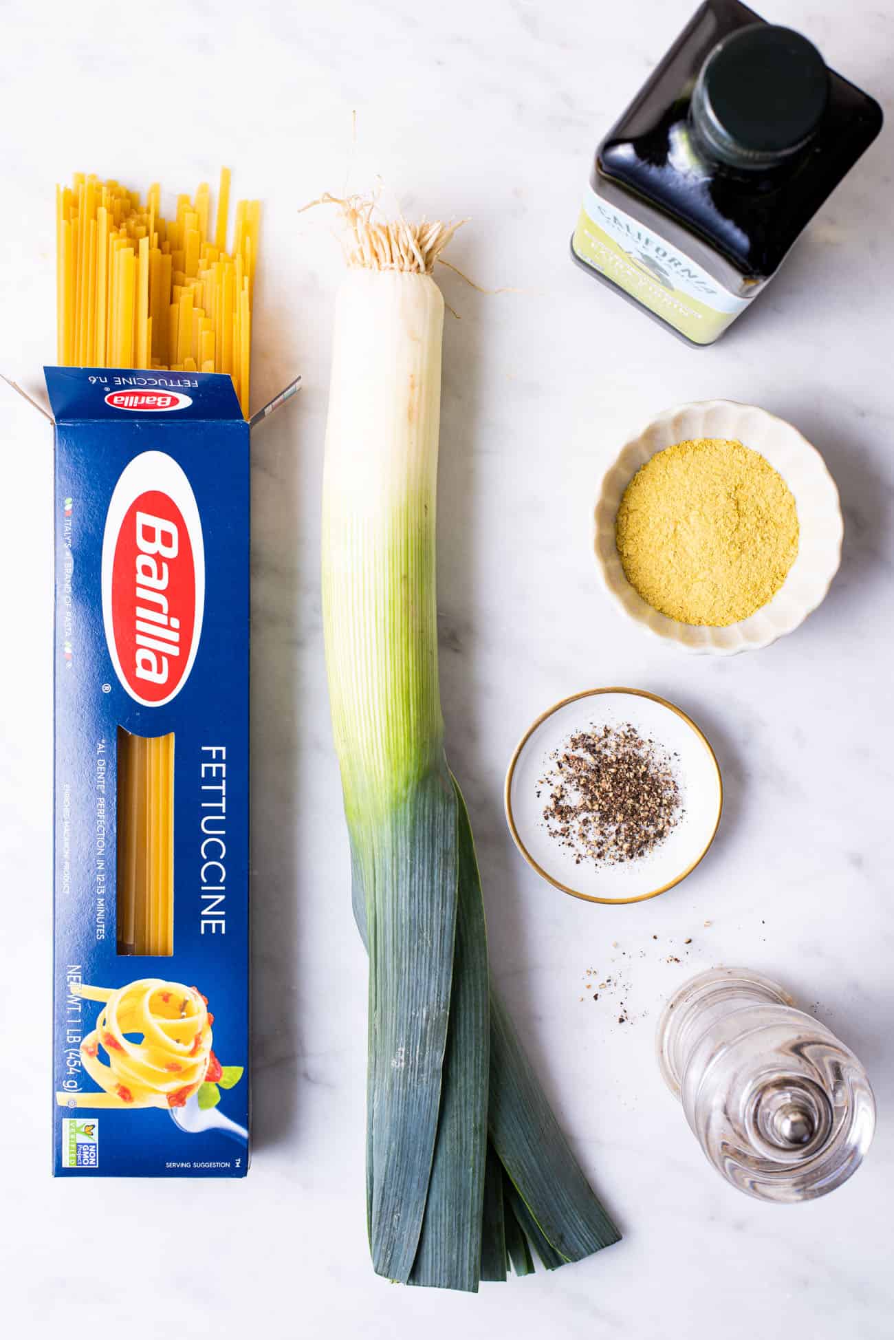 Barilla fettuccine, a leek, olive oil, nutritional yeast, and black pepper gathered on a marble counter