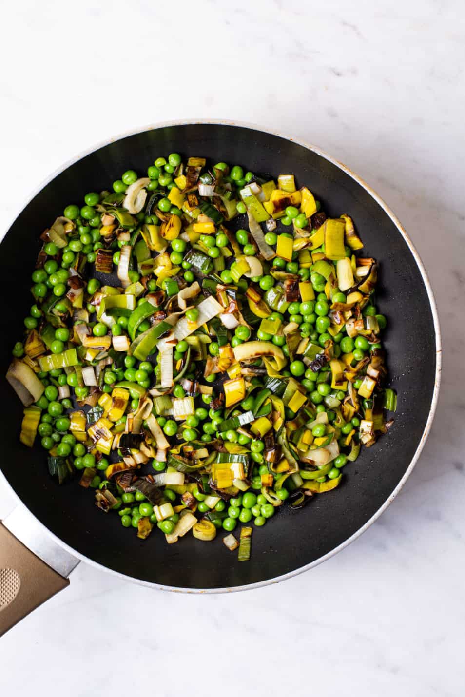 Fried leeks and peas in a skillet