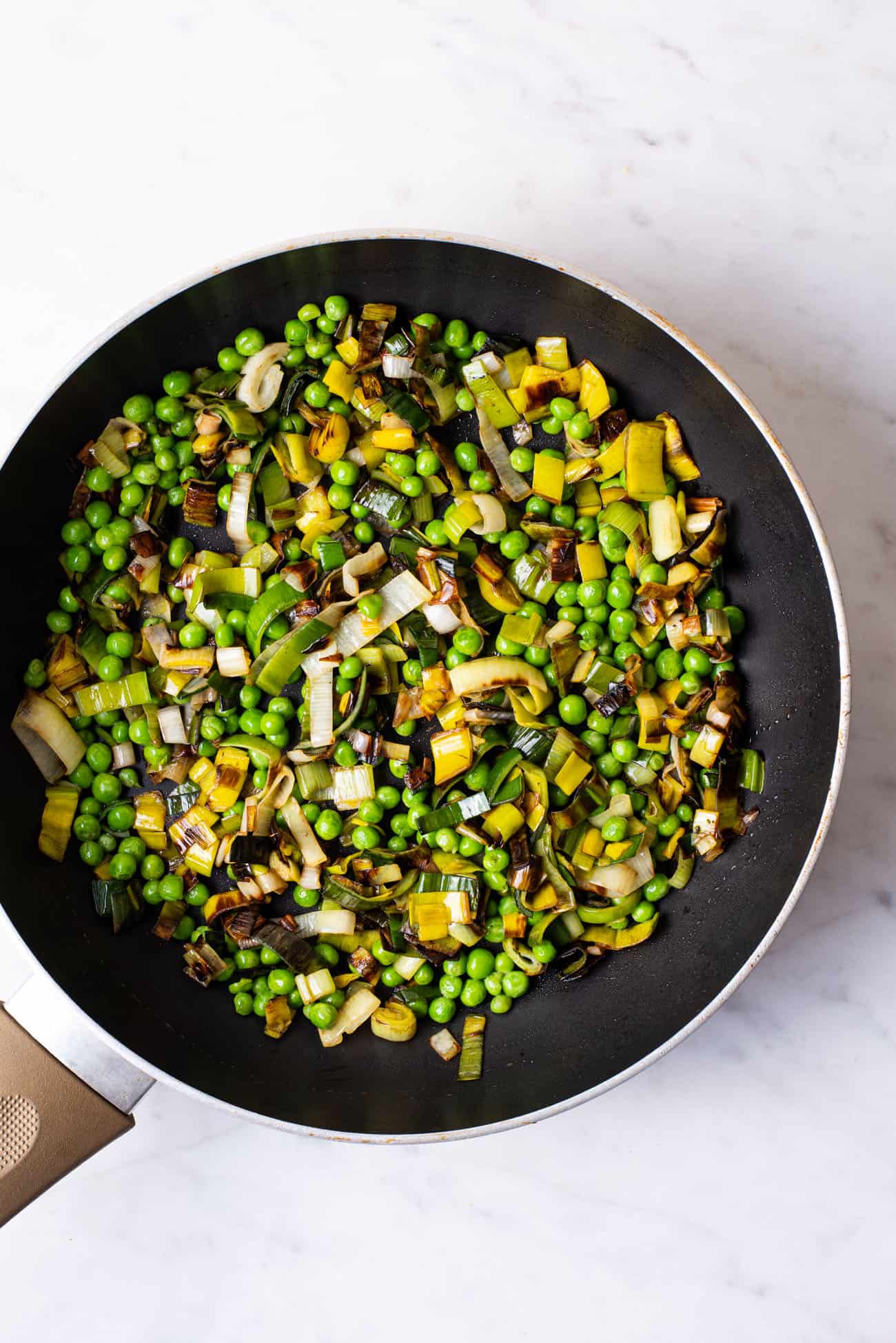 Fried leeks and peas in a skillet.