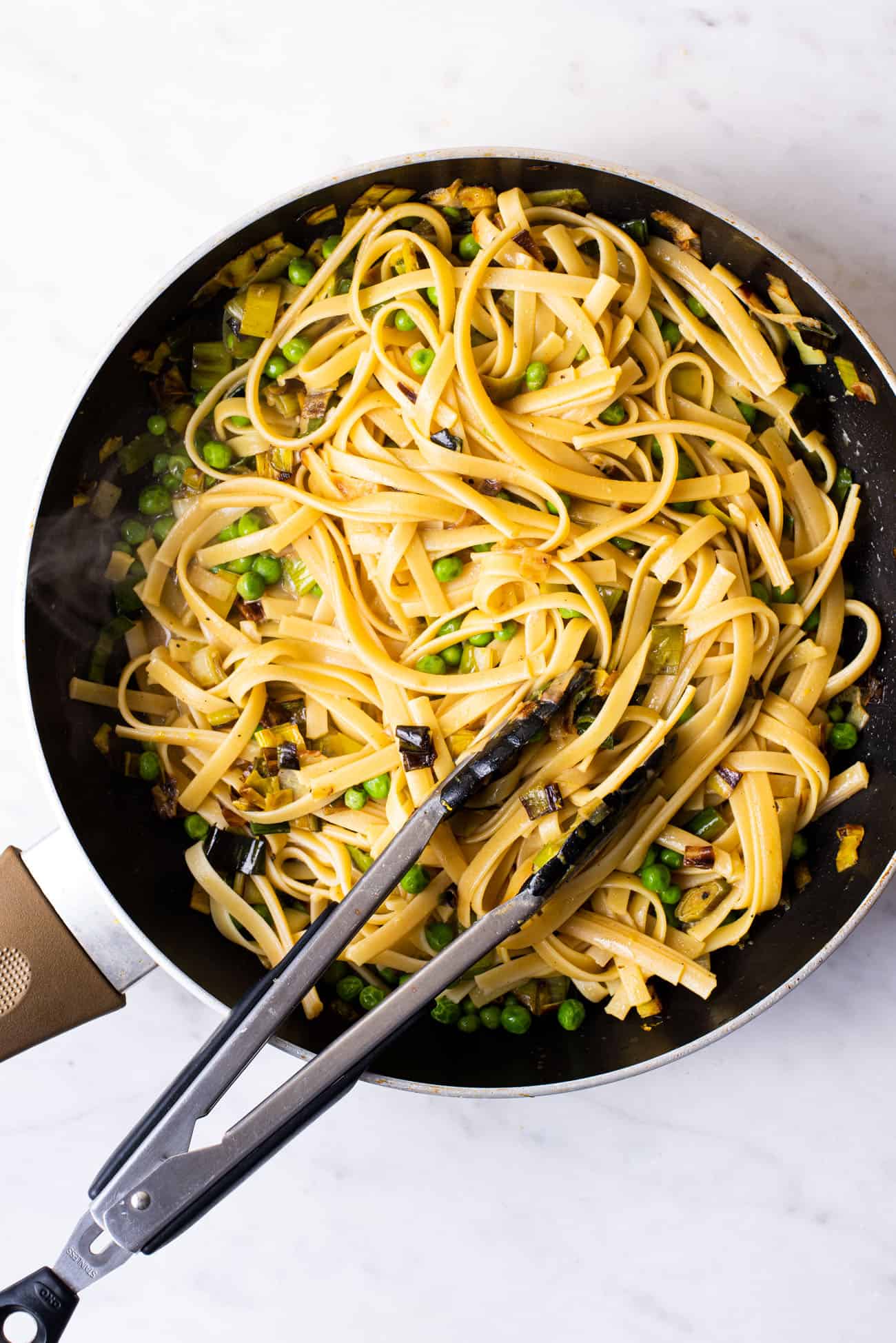 Vegan pasta with leeks and peas in a skillet with tongs.