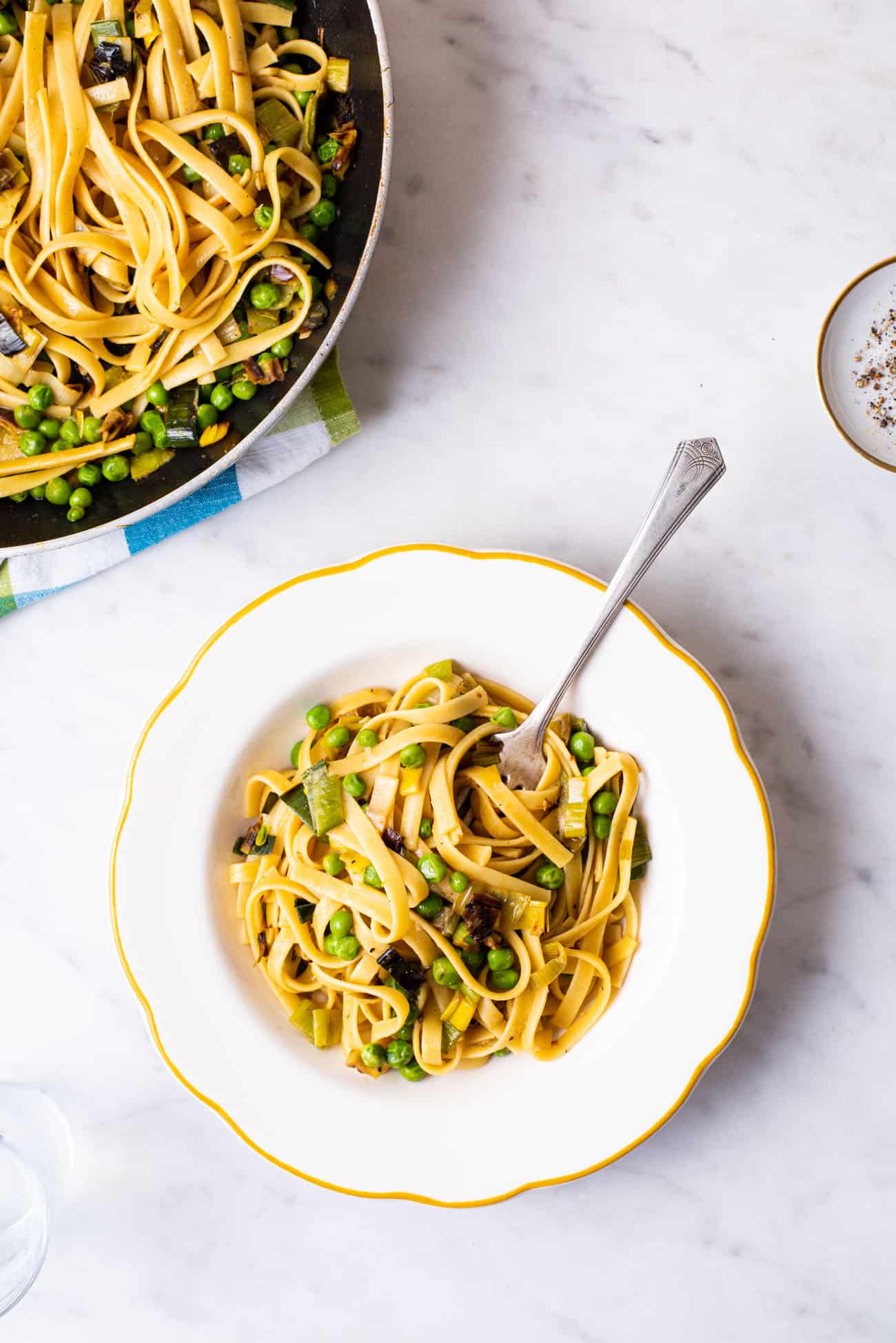 Vegan pasta with leeks and peas in a yellow-rimmed pasta bowl.