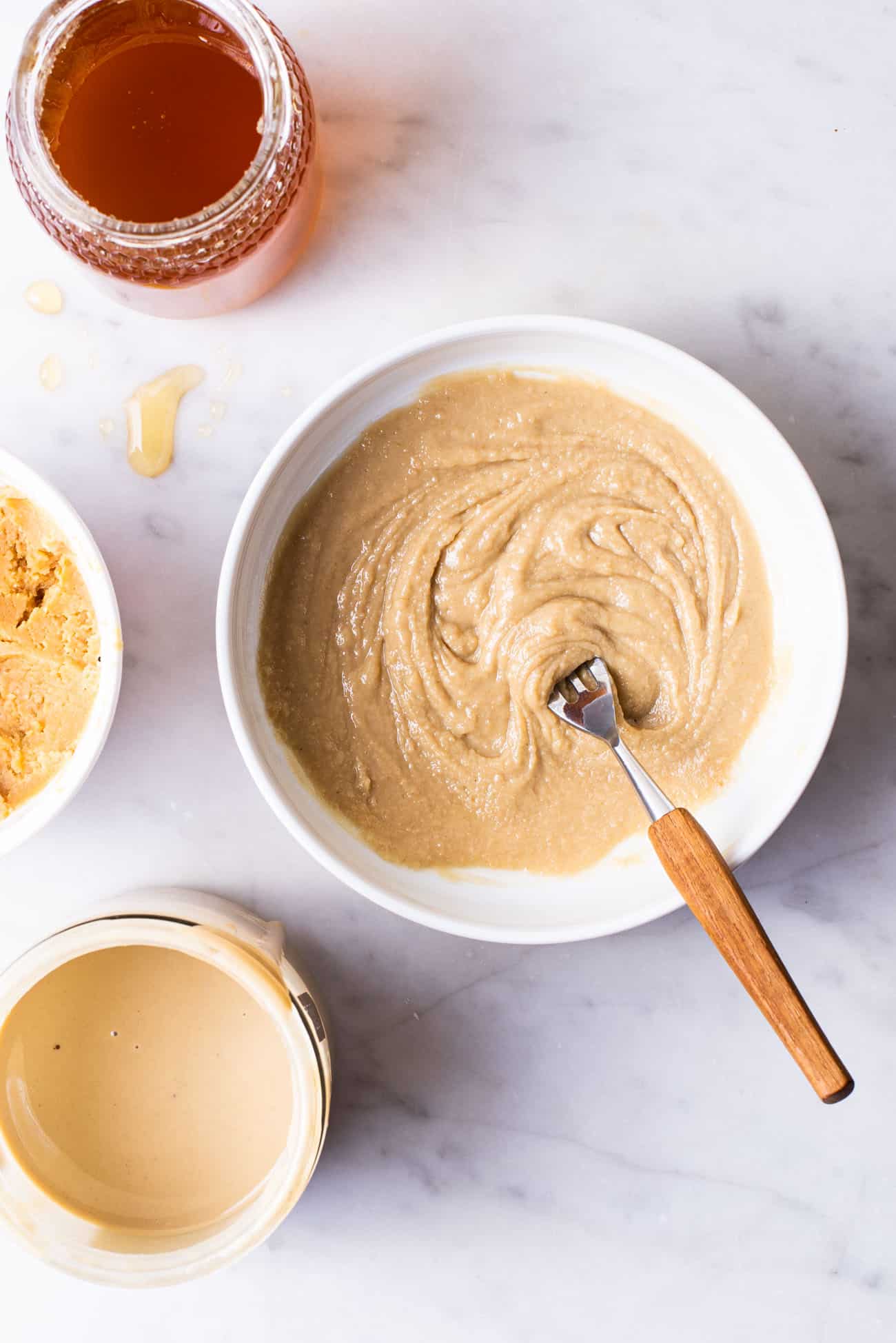 Tahini, miso and honey mixture in a white bowl with a fork.