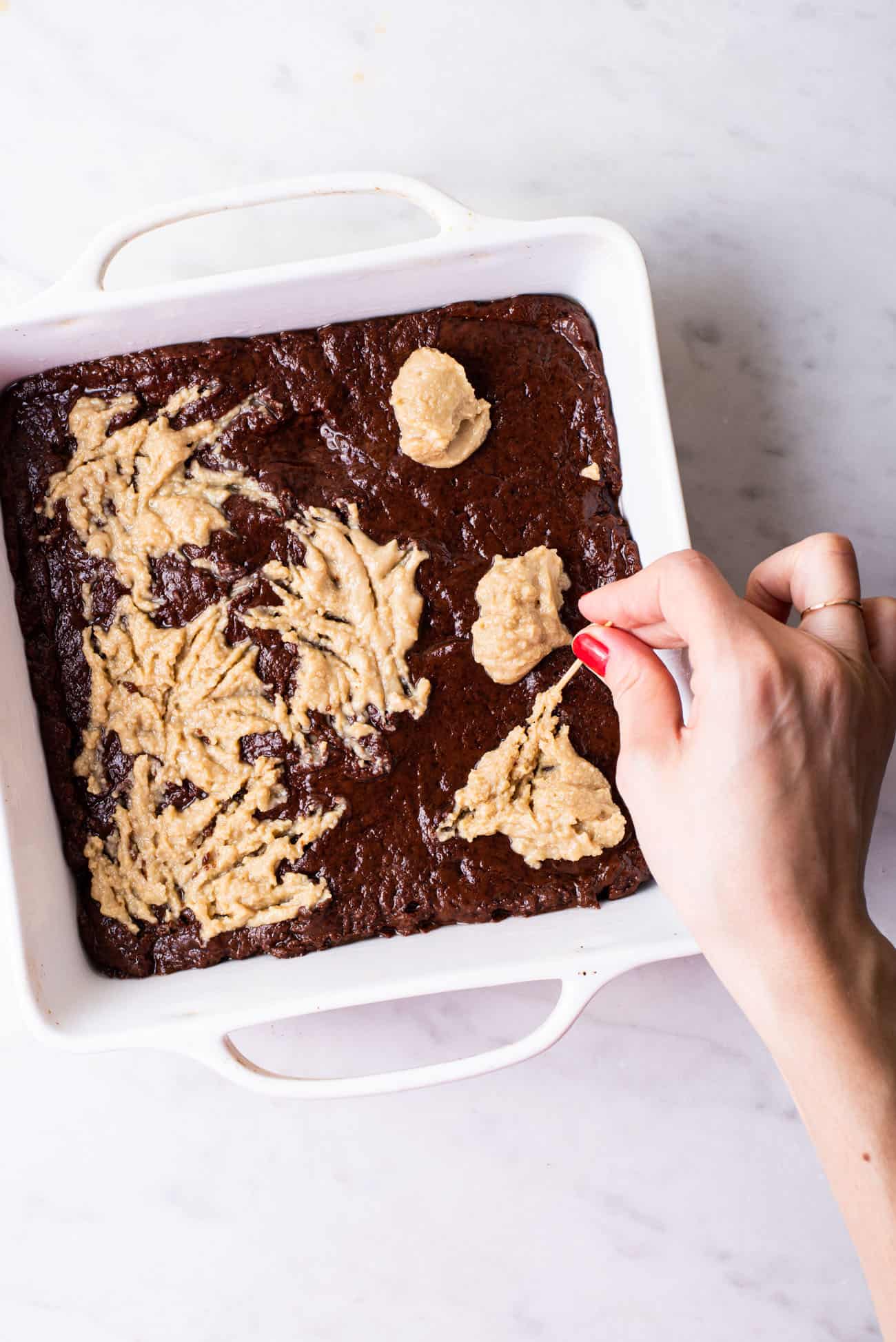 Woman's hand swirling tahini into brownie batter with a wooden toothpick.