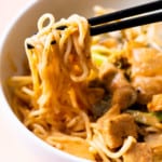 Close-up of black chopsticks holding creamy curry noodles