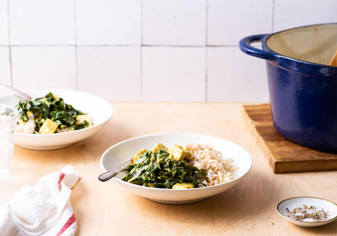 Vegan saag paneer in white bowls with brown basmati rice on a wooden counter with a tiled backsplash