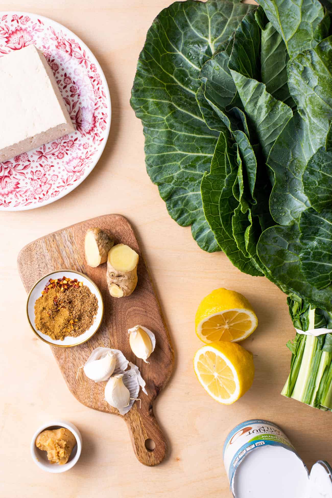 Tofu, collard greens, spices, miso, and lemon - all gathered on a wooden table