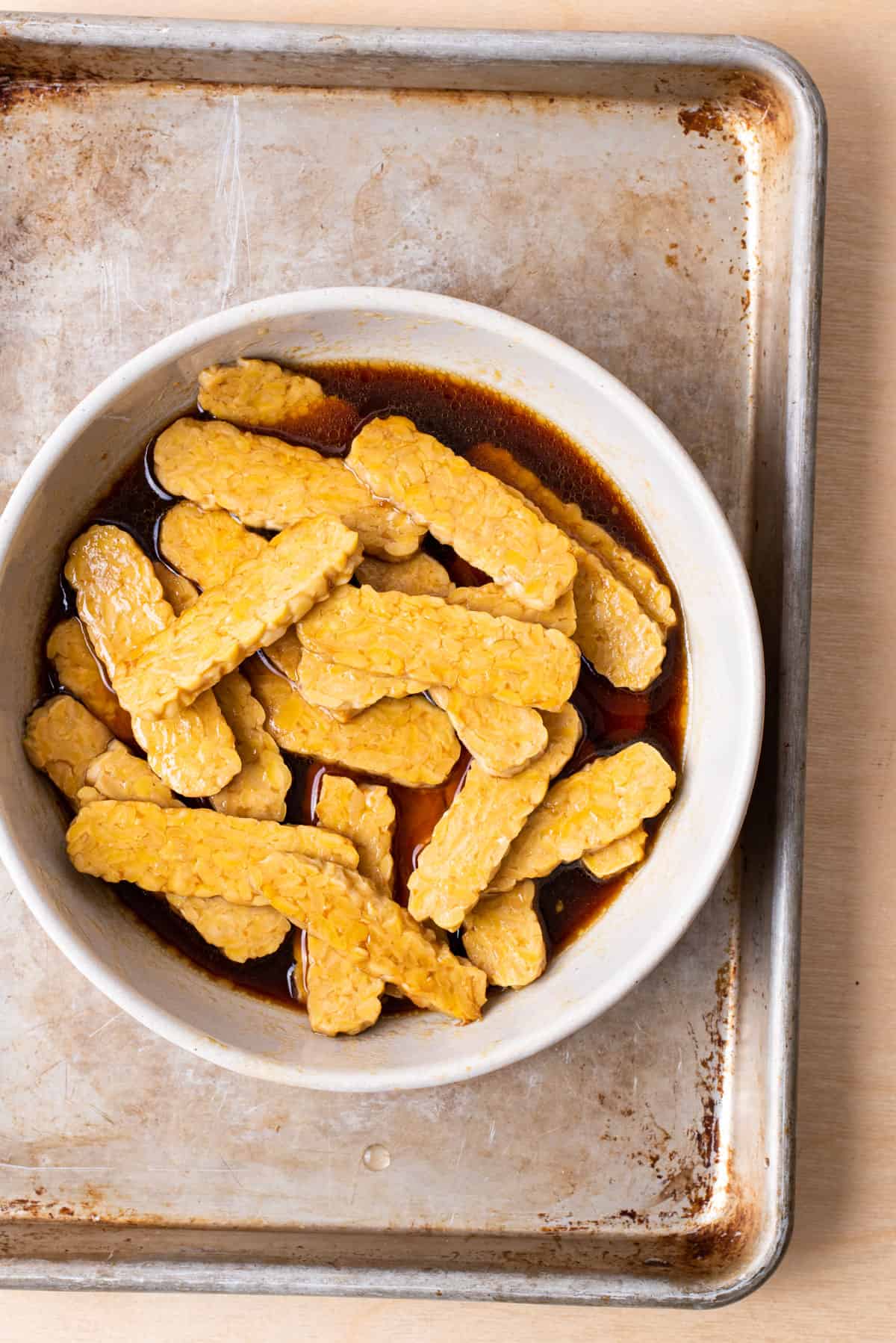 Tempeh slices marinating in a soy sauce-maple syrup mixture.