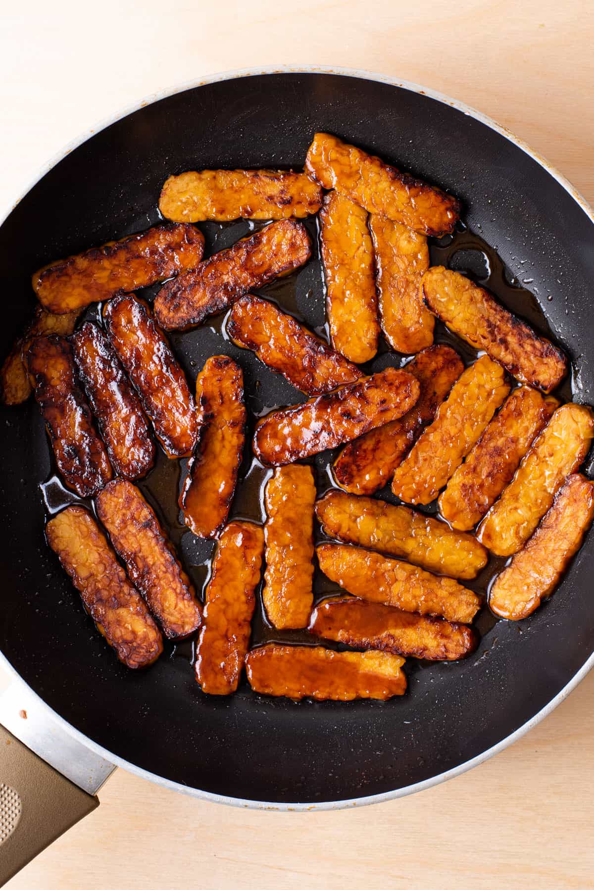 Soy-glazed tempeh slices cooking in a skillet.