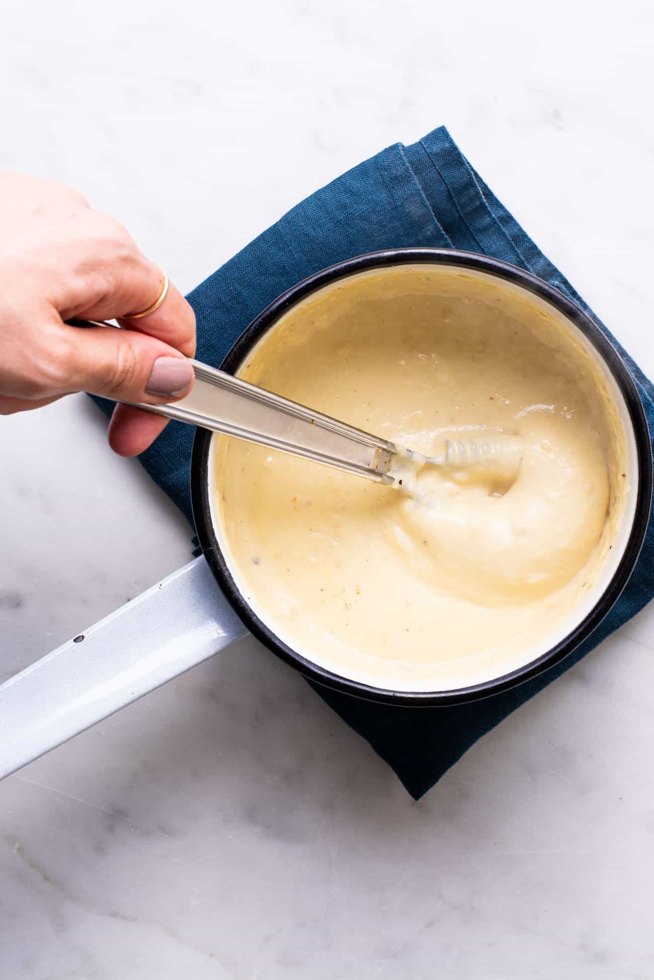 Thick and creamy, melty vegan cheese in a small pot with a whisk.