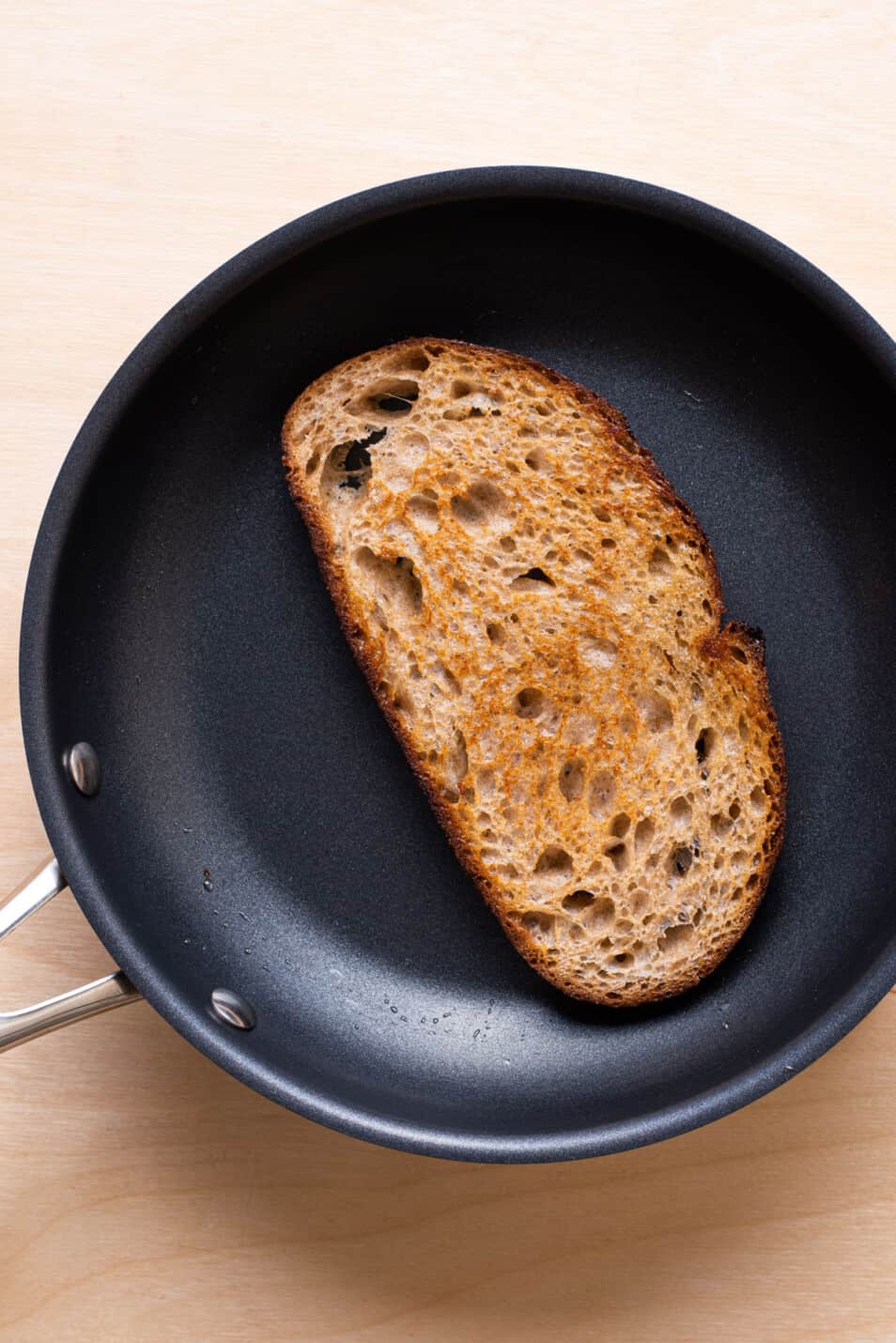 A slice of bread toasted in olive oil in a skillet.