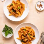 Two bowls of chickpea tomato pasta on a wooden table.