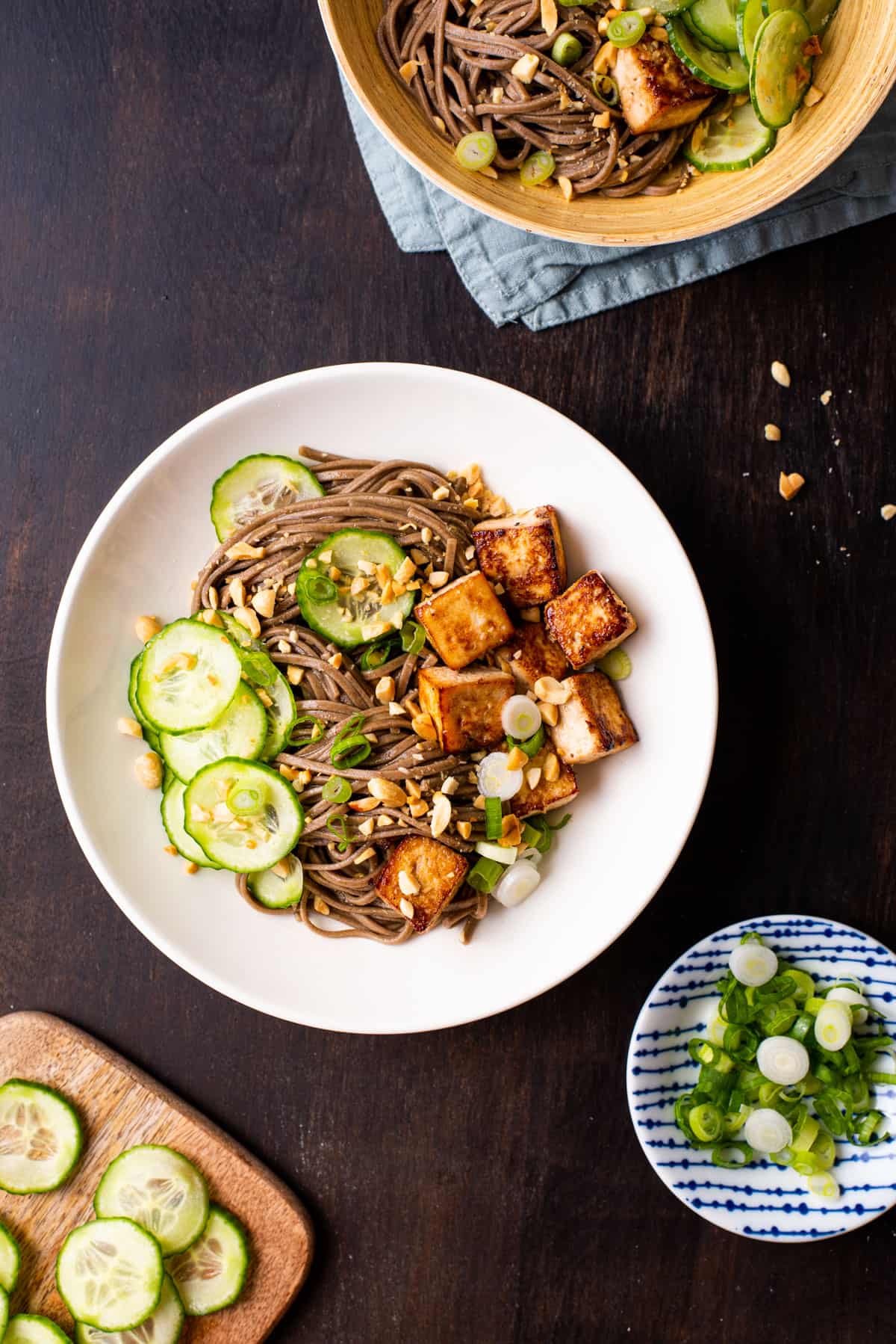 Vegan soba noodle bowl with tofu and cucumbers on a dark wooden table.