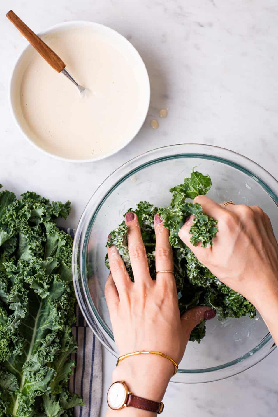 Woman's hands massaging kale with tahini dressing.