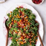 Massaged kale salad with crispy chickpeas on an oval platter next to pomegranate seeds.