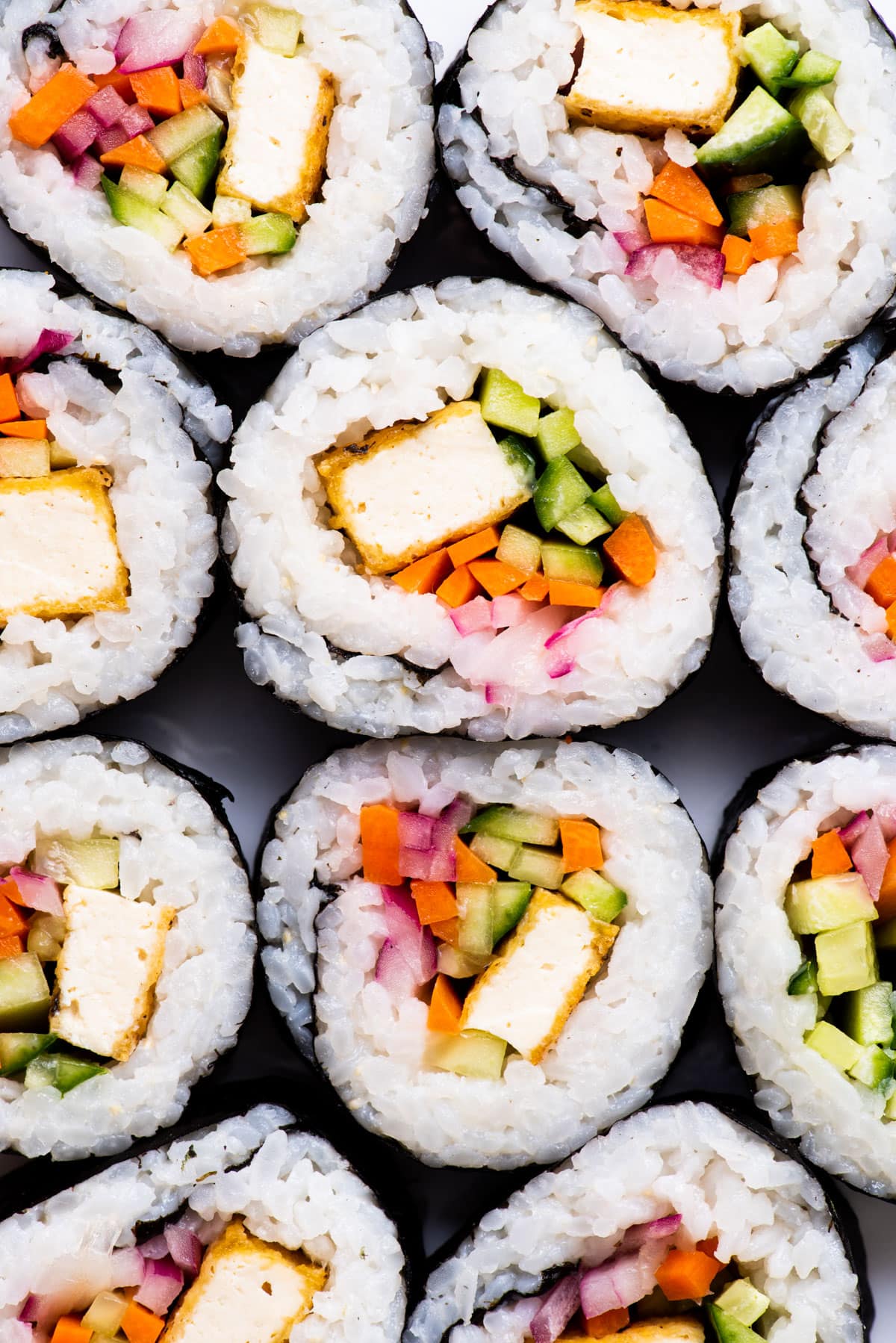 Close-up of vegan sushi rolls with white rice, crispy tofu, carrots, and cucumbers.