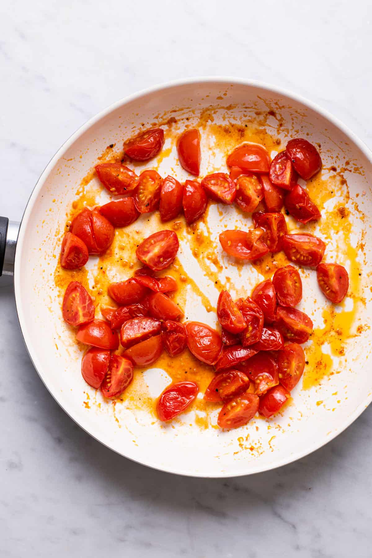 Juicy sautéed tomatoes in a white skillet.