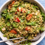 Summer rice salad with pesto and tomatoes in a beige bowl on a blue napkin.