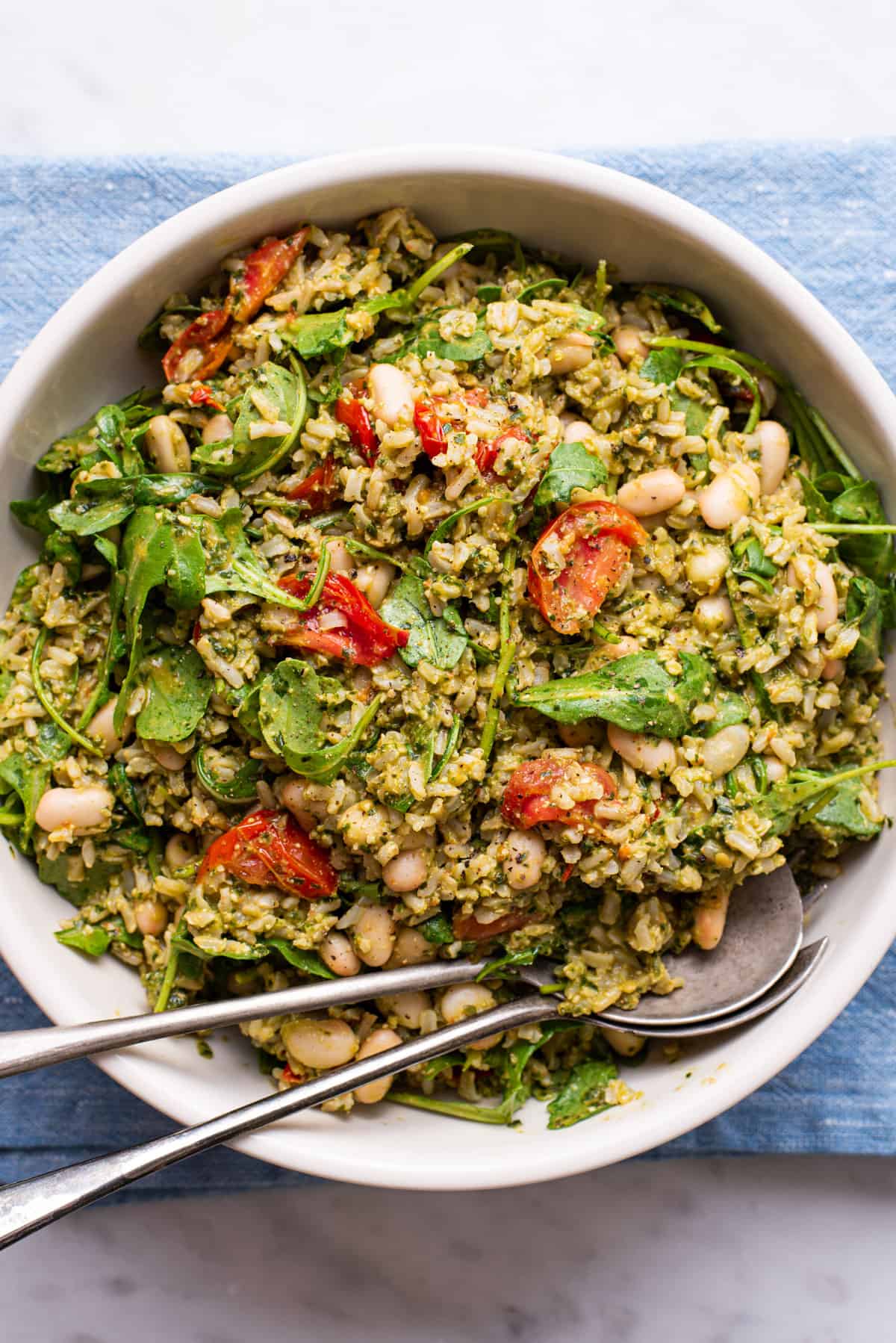 Summer rice salad with pesto and tomatoes in a beige bowl on a blue napkin.