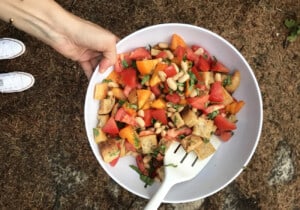 Woman's hand holding a bowl of panzanella while camping.