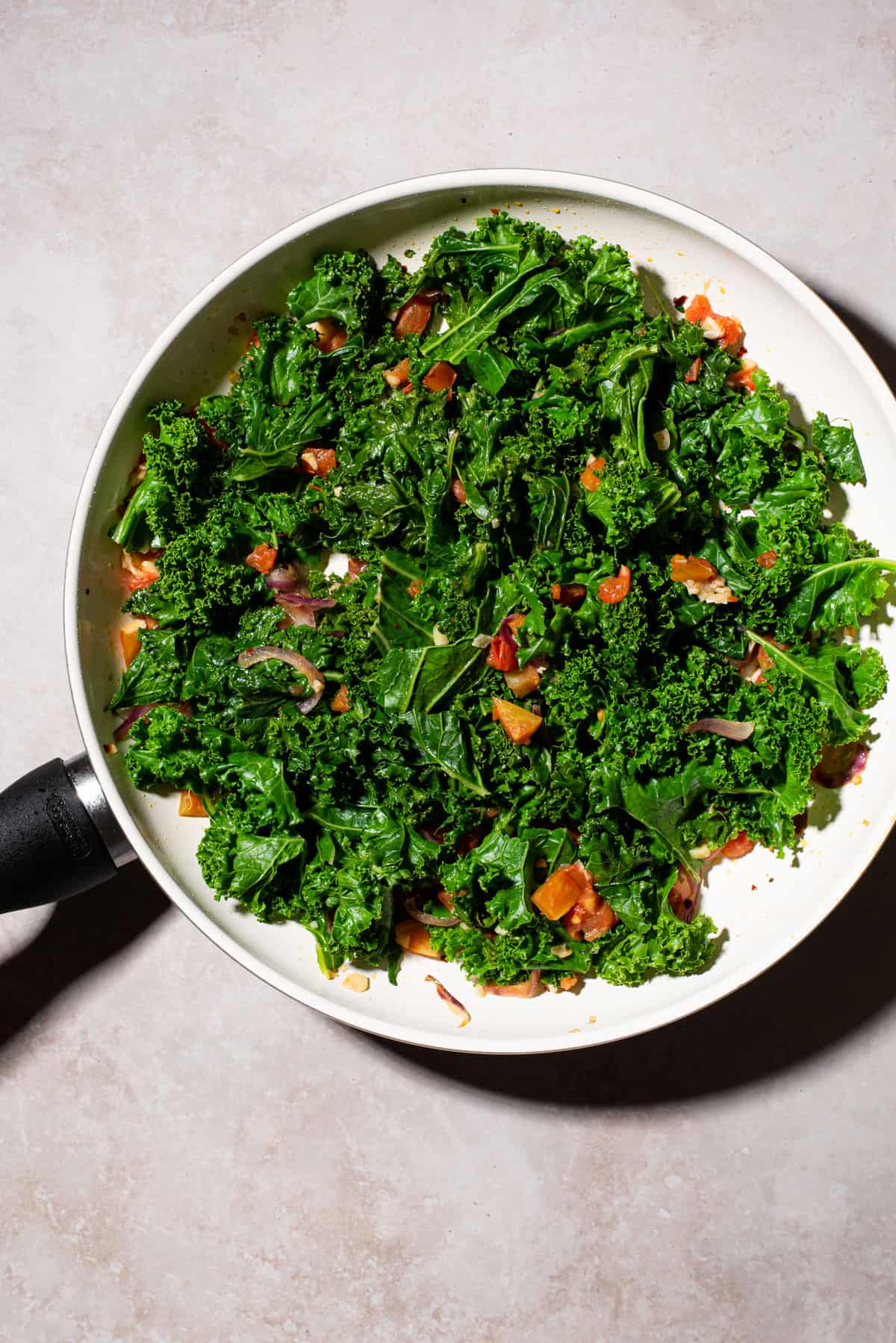 Sautéed kale with tomatoes in a skillet.