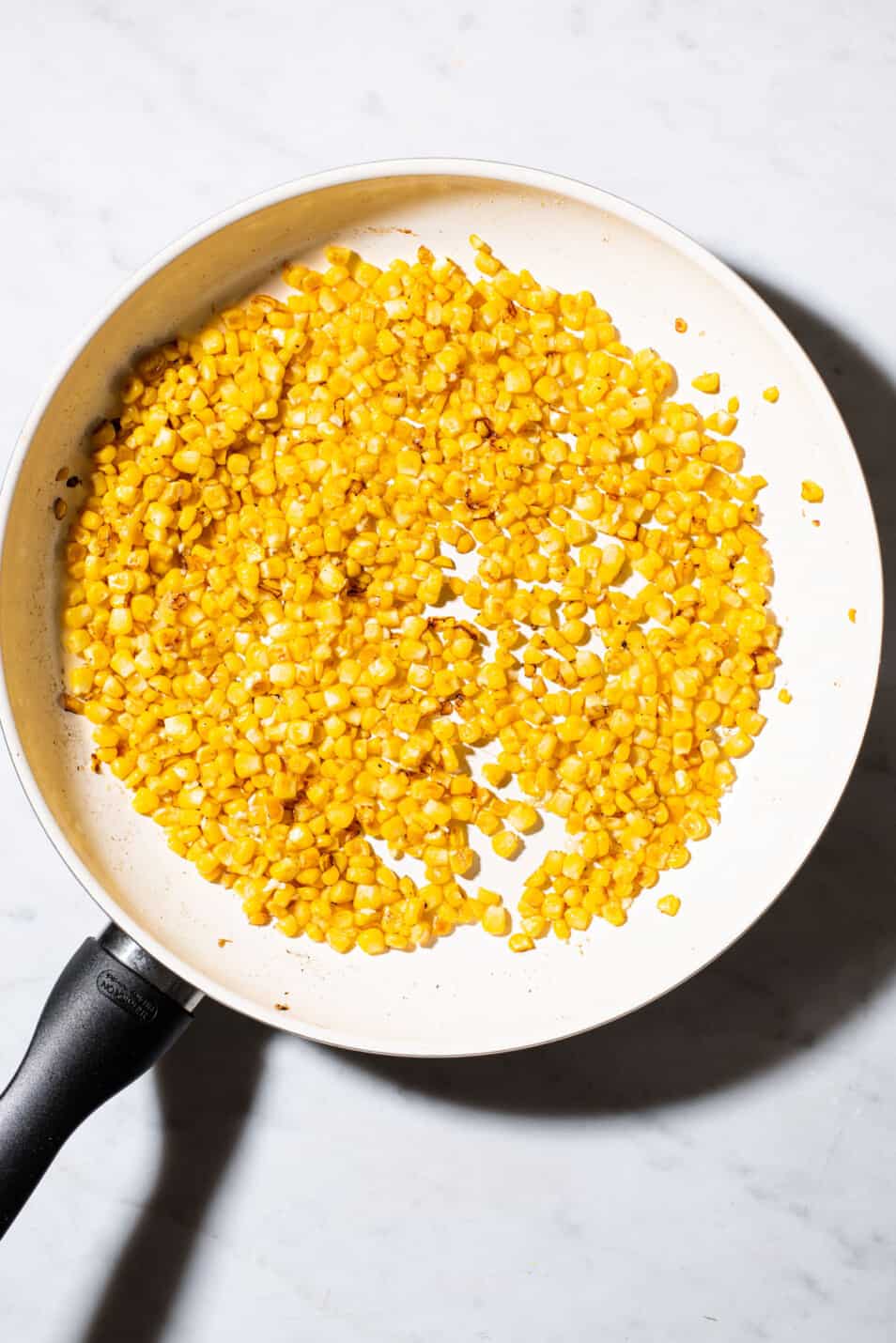 Sautéed corn kernels in a white skillet.