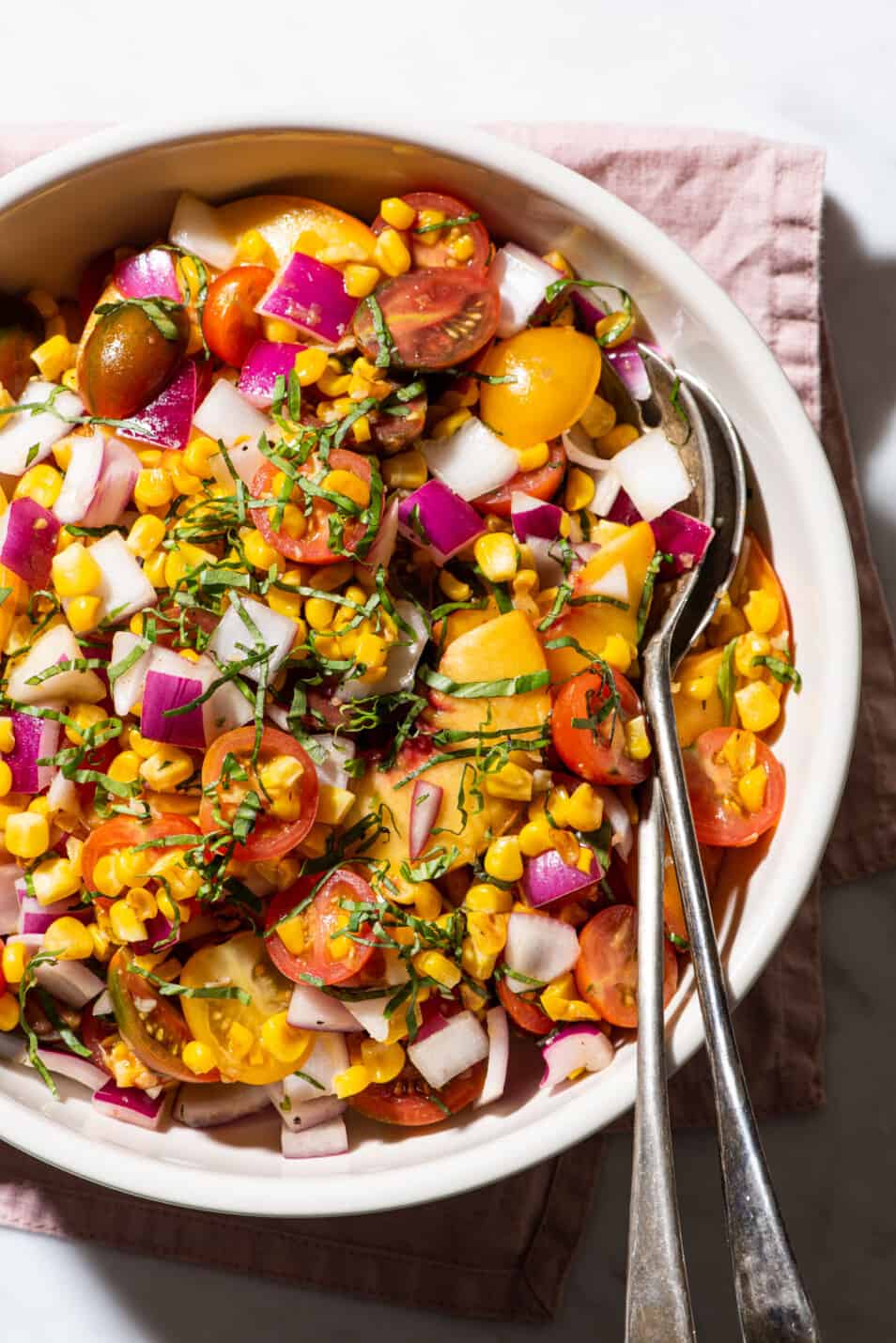 A healthy summer salad consisting of tomatoes, peaches, red onion, corn, and basil.