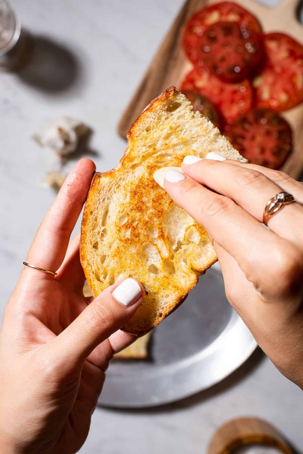 Woman's hands rubbing raw garlic on sourdough toast.