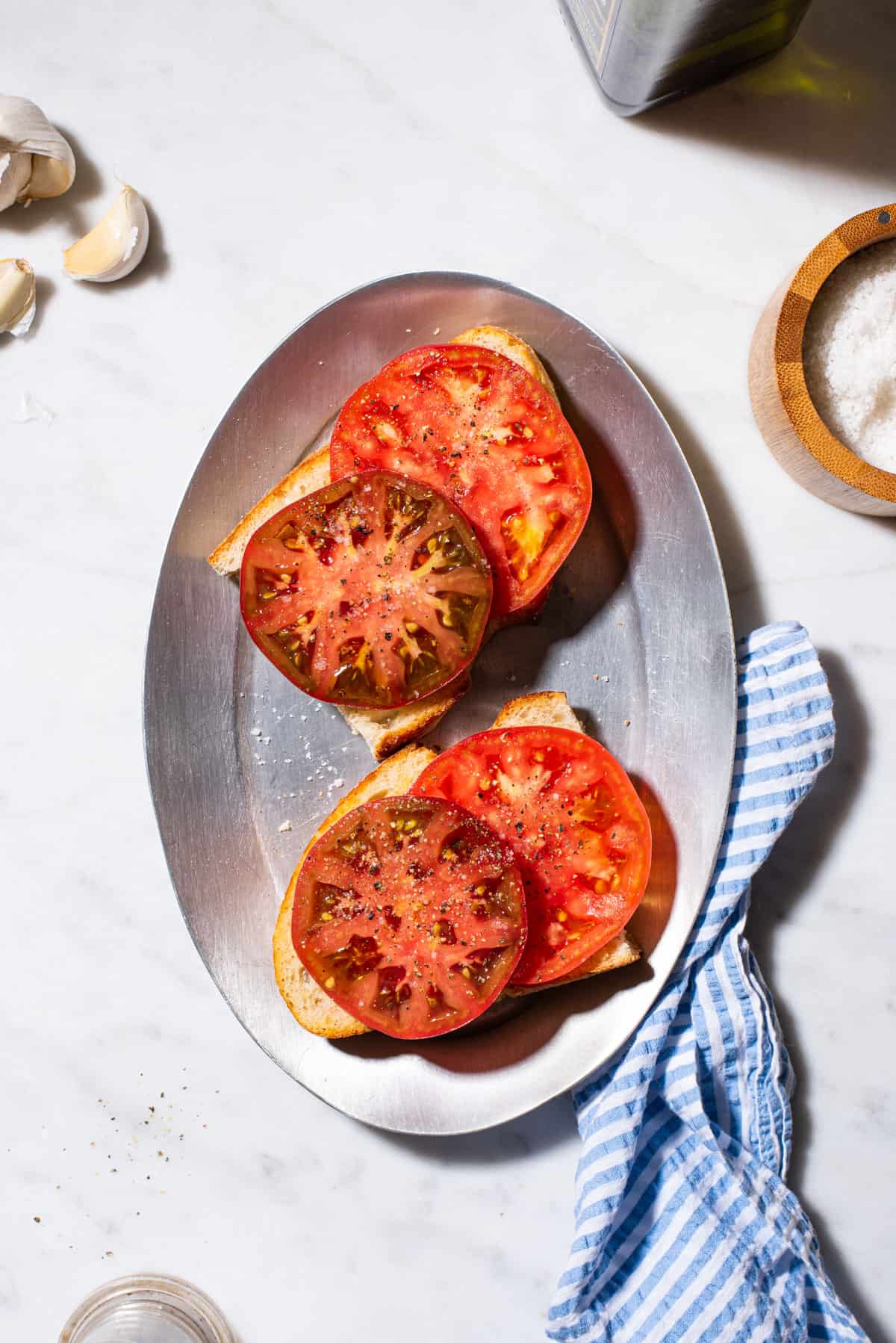 2 pieces of garlicky heirloom tomato toast on a sizzle plate next to a blue striped towel.