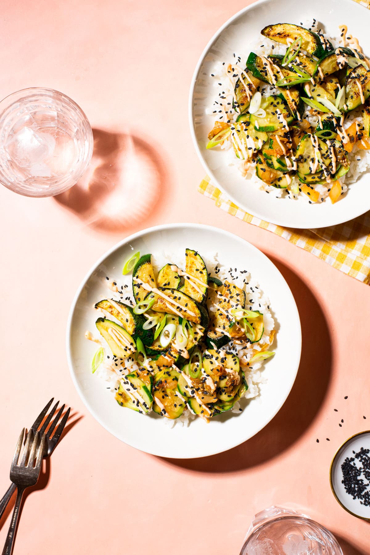 Veggie poke bowls with sautéed zucchini on a pink table.