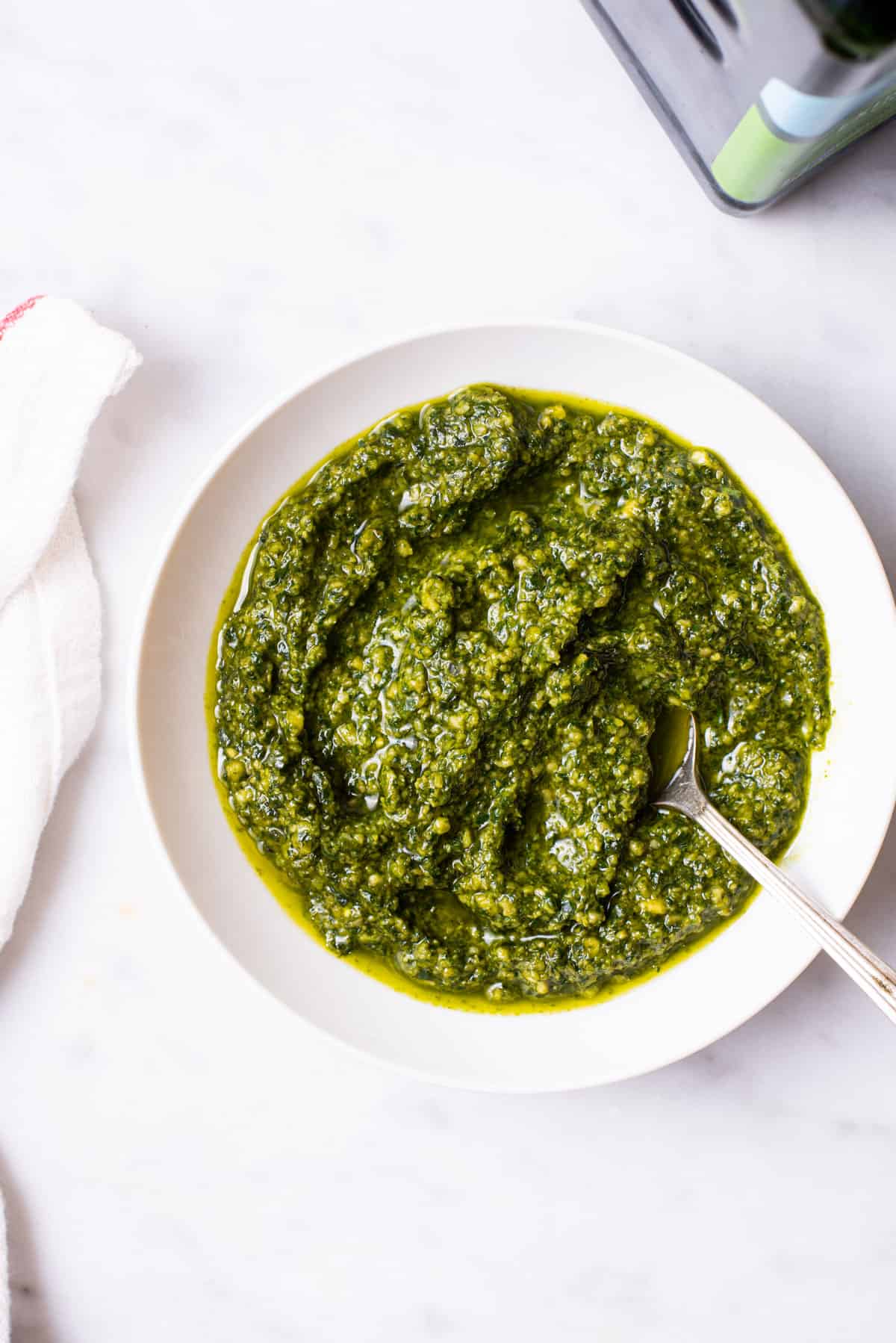 Homemade dairy-free pesto in a white bowl on a marble table.