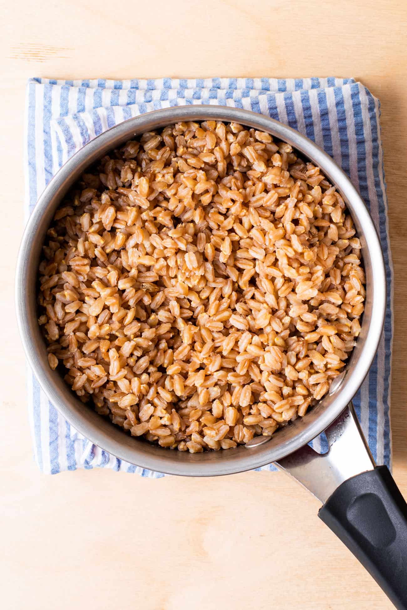 Small pot of cooked farro on a blue striped towel.