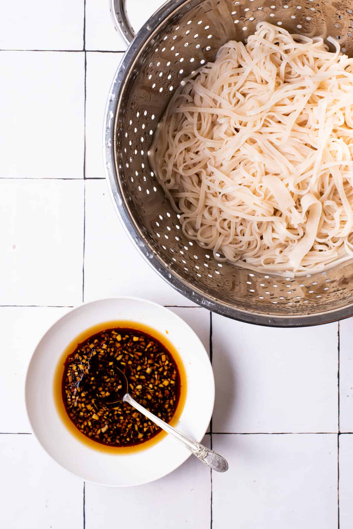 Drained rice noodles in a colander next to stir fry sauce.