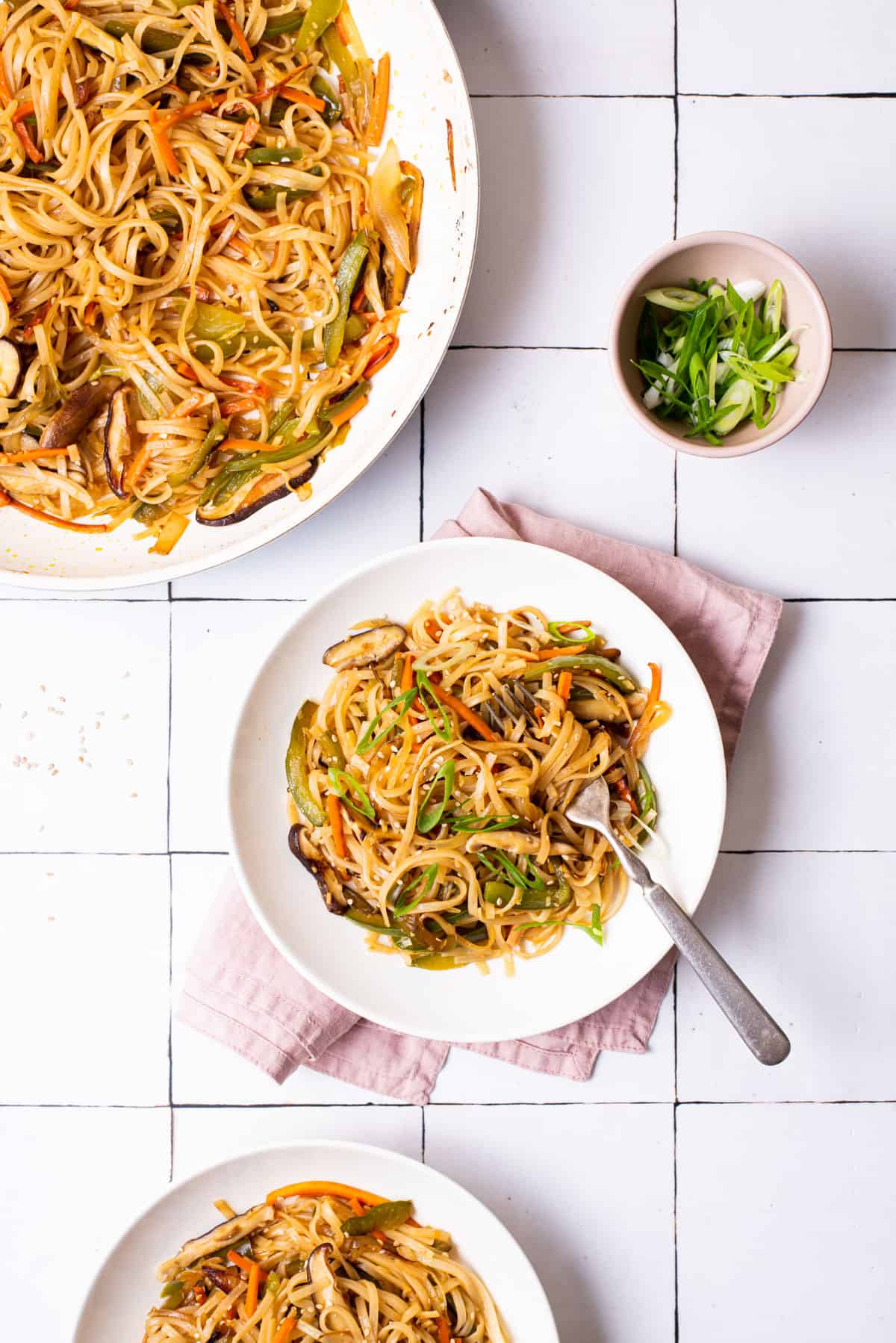 Bowl of stir fried noodles with vegetables next to sliced scallions.